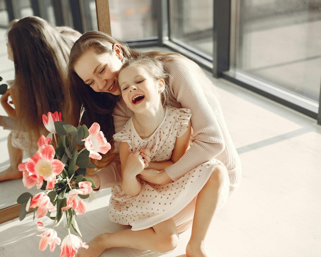 A mother and her daughter laughing together while holding a bouquet of pink tulips